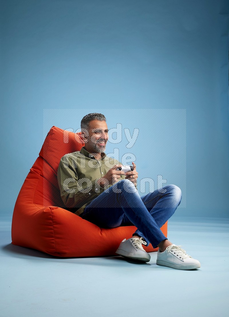 A man sitting on an orange beanbag and gaming with joystick