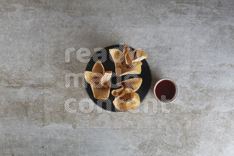wonton cups with soy sauce ramkin on circle slate on grey textured counter top