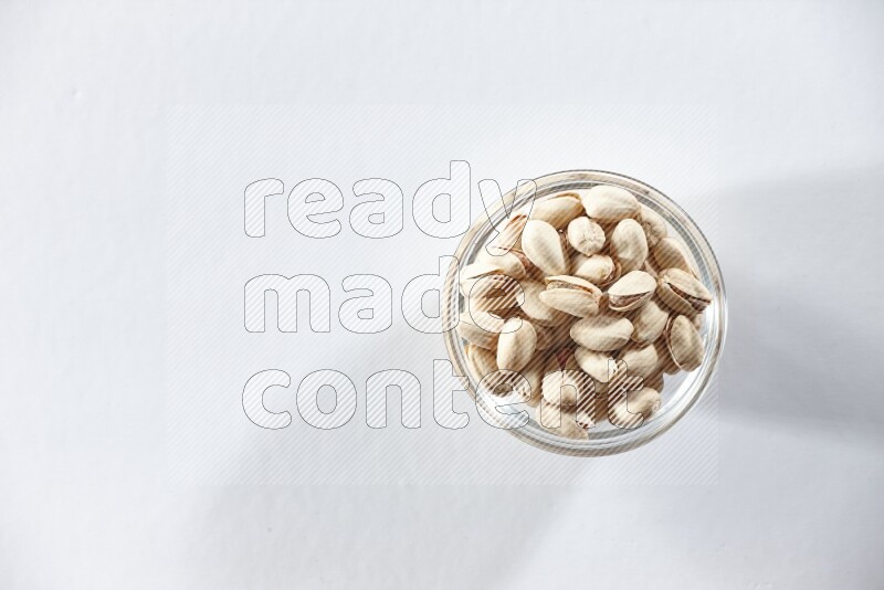 A glass bowl full of pistachios on a white background in different angles