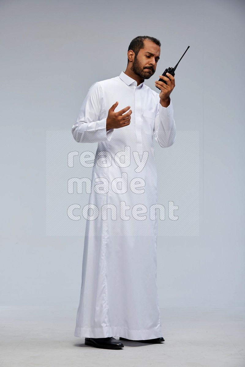 Saudi man Wearing thob standing holding walkie-talkie on Gray background
