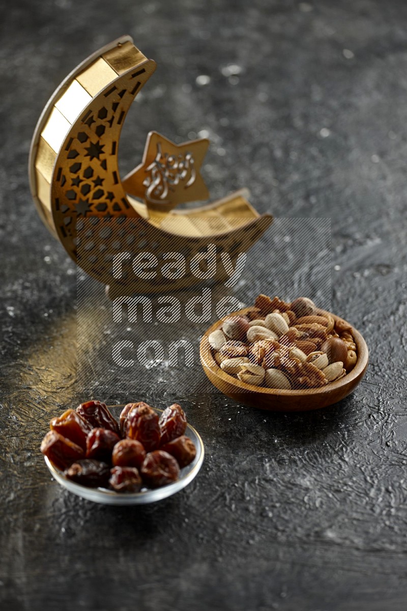 A wooden golden crescent lantern with different drinks, dates, nuts, prayer beads and quran on textured black background