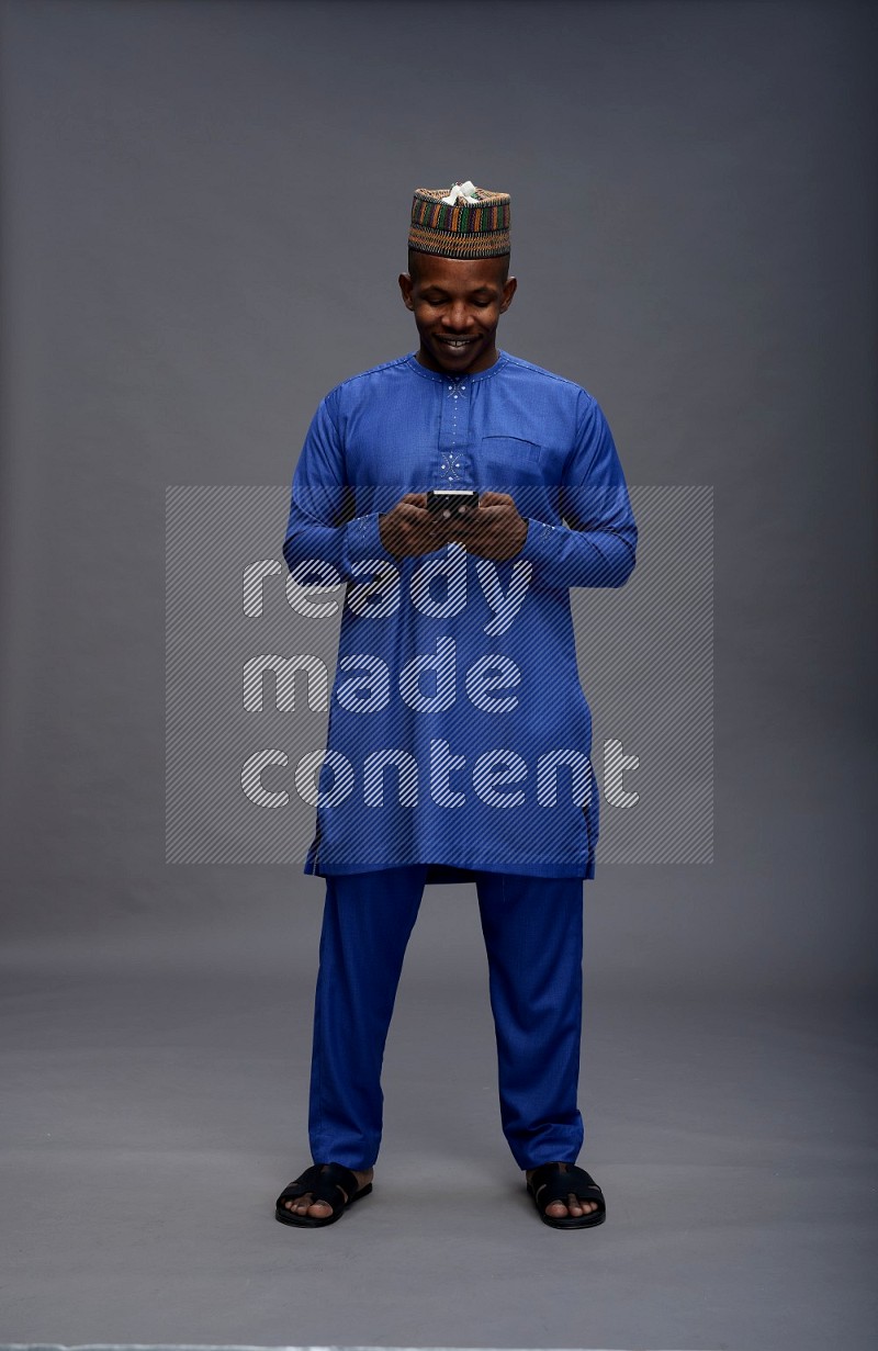Man wearing Nigerian outfit standing texting on phone on gray background