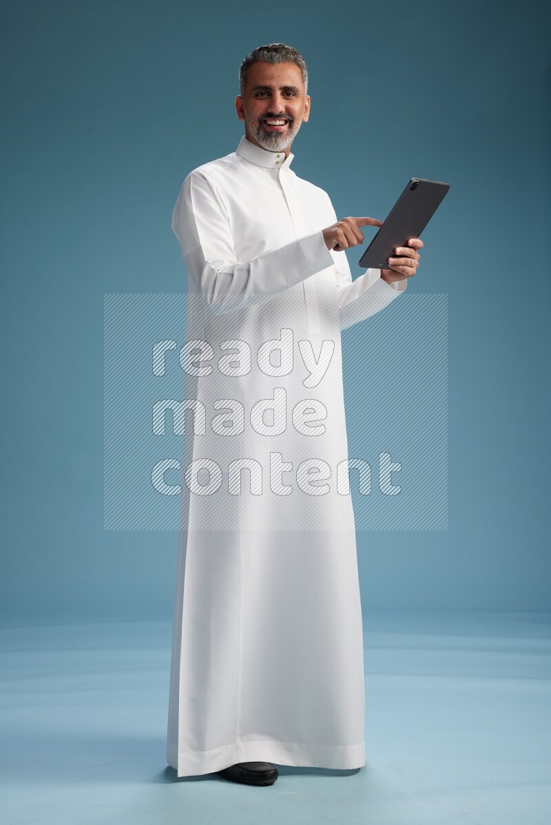 Saudi man waring thob with tablet on blue background