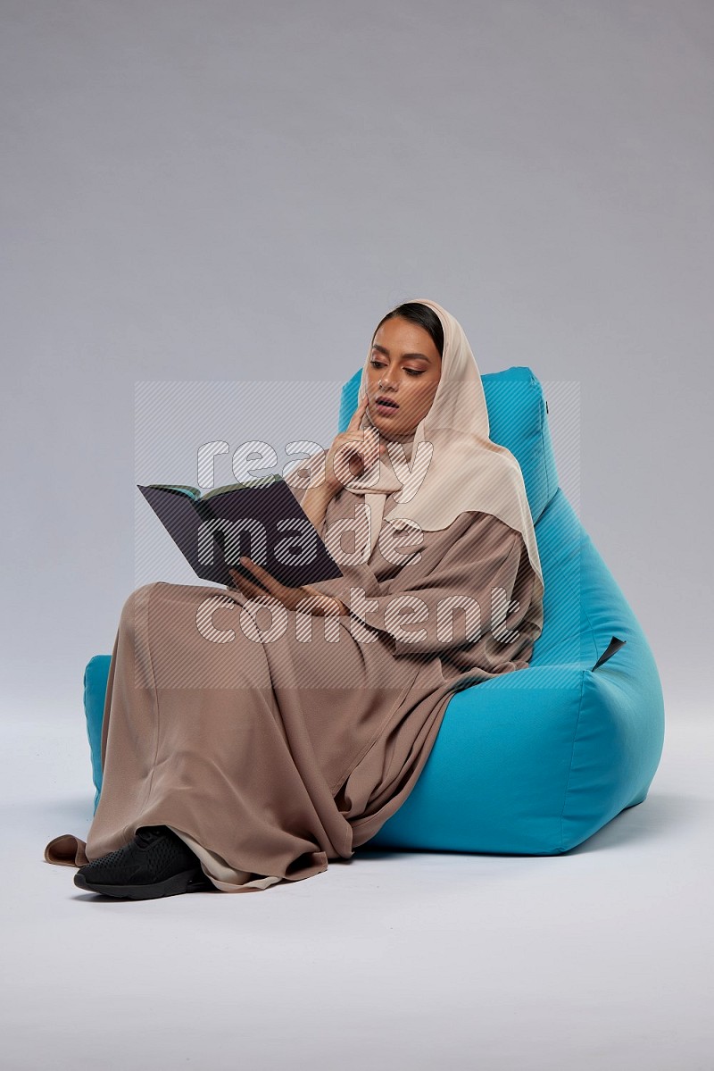 A woman sitting on a blue beanbag and reading a book