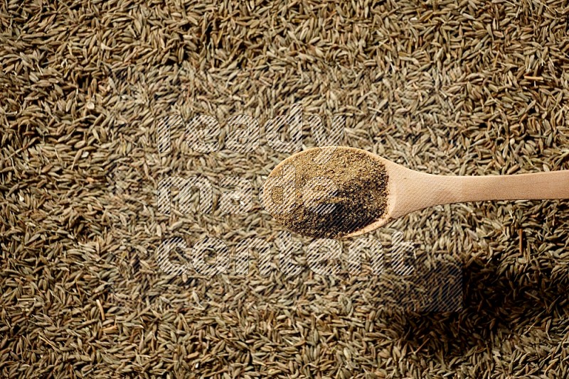 A wooden spoon full of cumin powder on a cumin seeds background