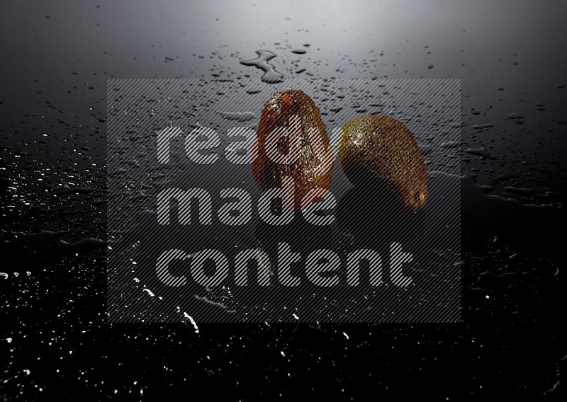 A whole avocado on black background with water drops.