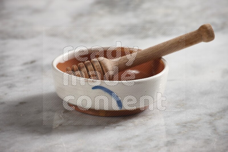 Multicolored pottery bowl with wooden honey dipper in it on grey marble background