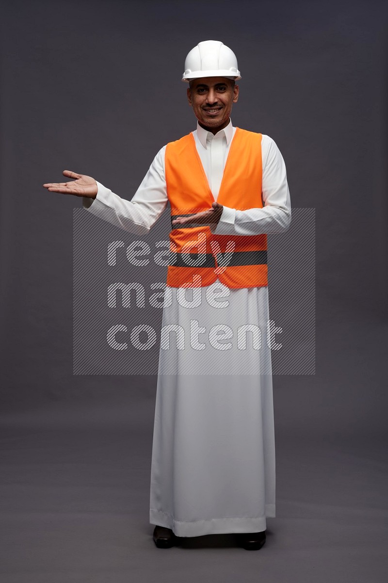 Saudi man wearing thob with engineer vest standing interacting with the camera on gray background