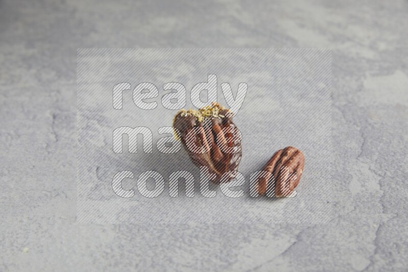 pecan stuffed date covered with Dark chocolate and chopped pistachios on alight grey background