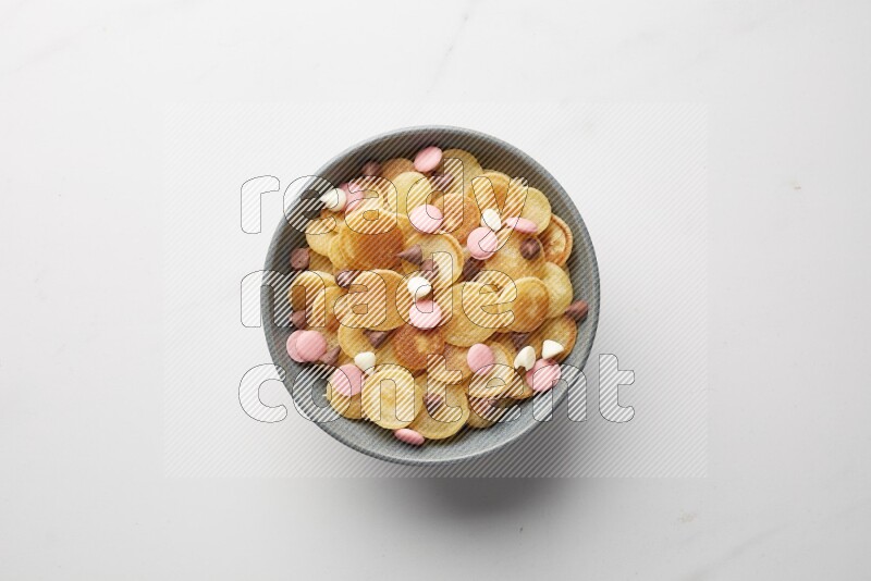Top-view shot of mixed chocolate chips cereal pancakes in a round bowl on white background