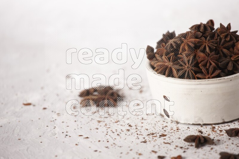 Star Anise in a white bowl and more of it sprinkled on white background