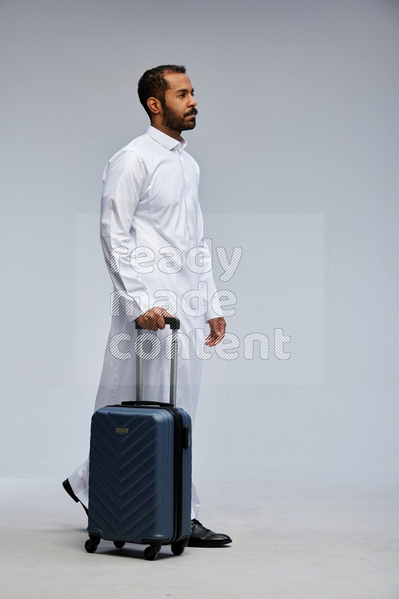 Saudi man wearing thob standing holding Travel bag on Gray background