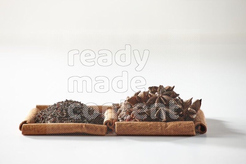 مربعان من أعواد القرفة ممتلئان باليانسون النجمي والشاي الأسود علي خلفية بيضاء