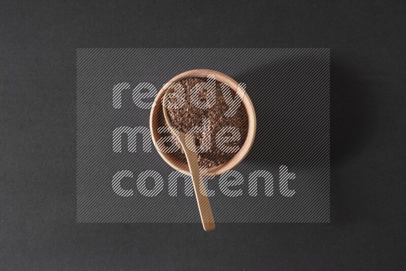 وعاء خشبي ممتلئ بحبوب بذر الكتان مع ملعقة خشبية ممتلئة بالحبوب علي خلفية سوداء