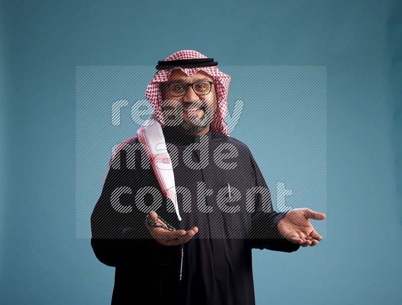 Saudi Man with shimag Standing Interacting with the camera on blue background