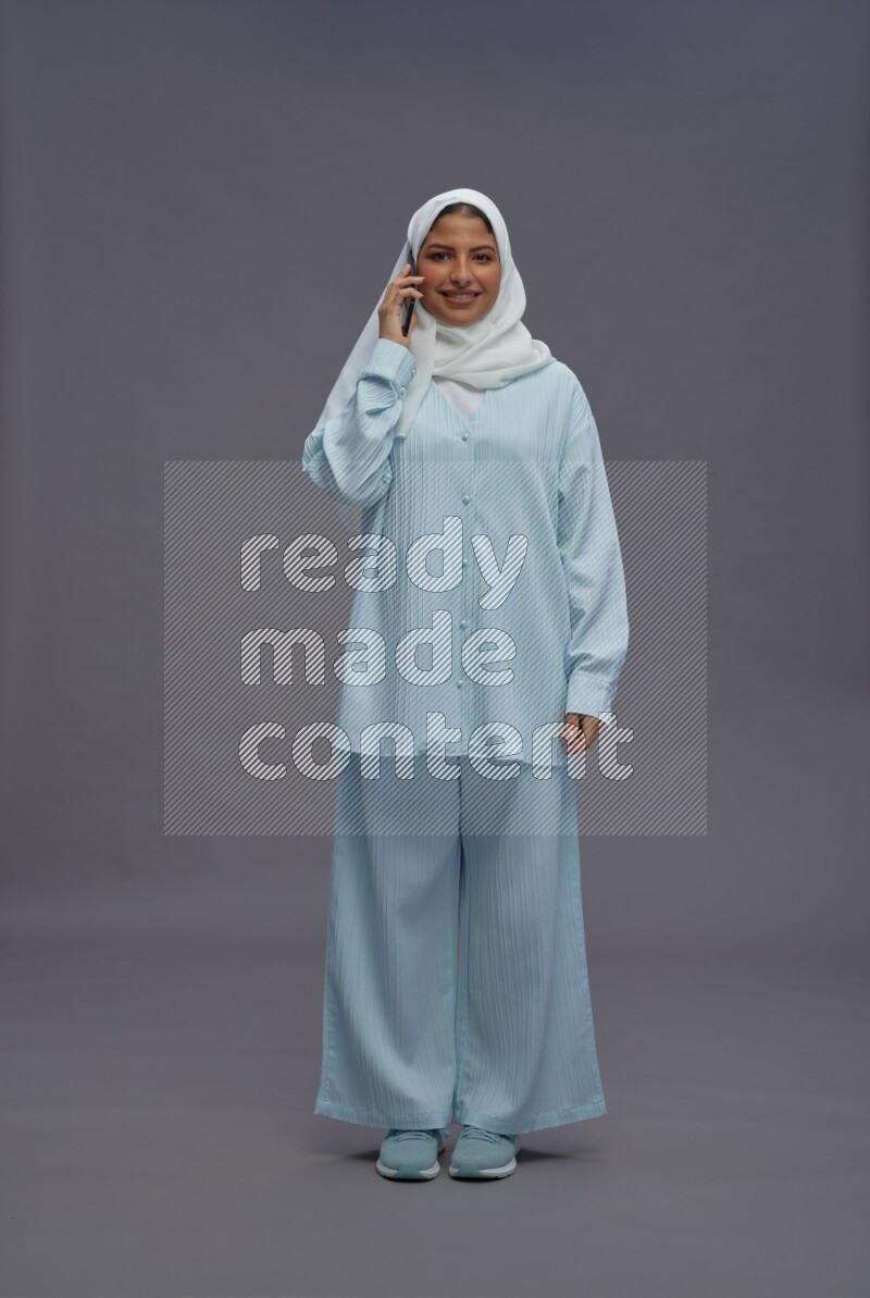 Saudi woman wearing hijab clothes standing talking on phone on gray background