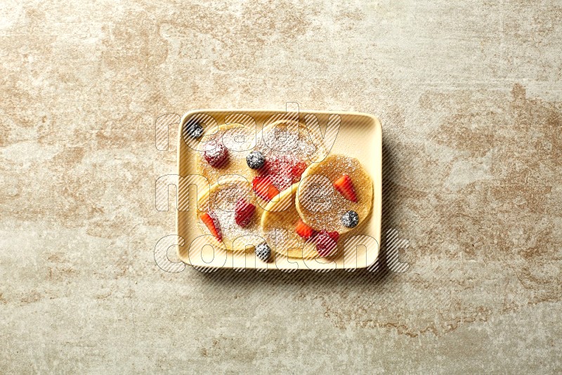 Five stacked mixed berries mini pancakes in a rectangular plate on beige background