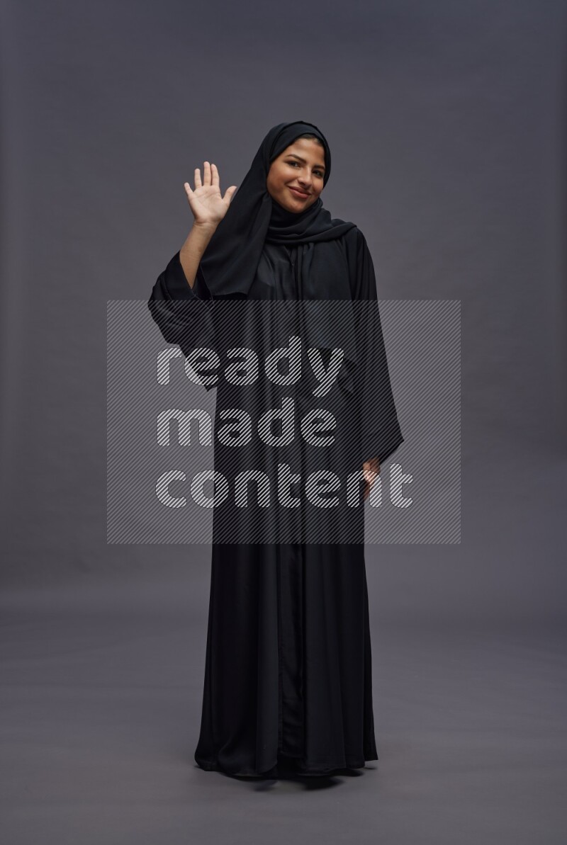 Saudi woman wearing Abaya standing interacting with the camera on gray background