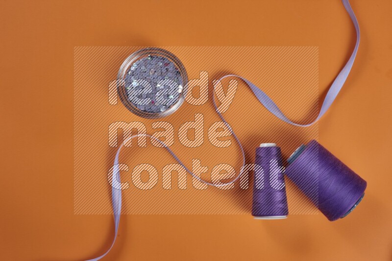 A purple collection of sewing and tailoring tools arranged on a orange background