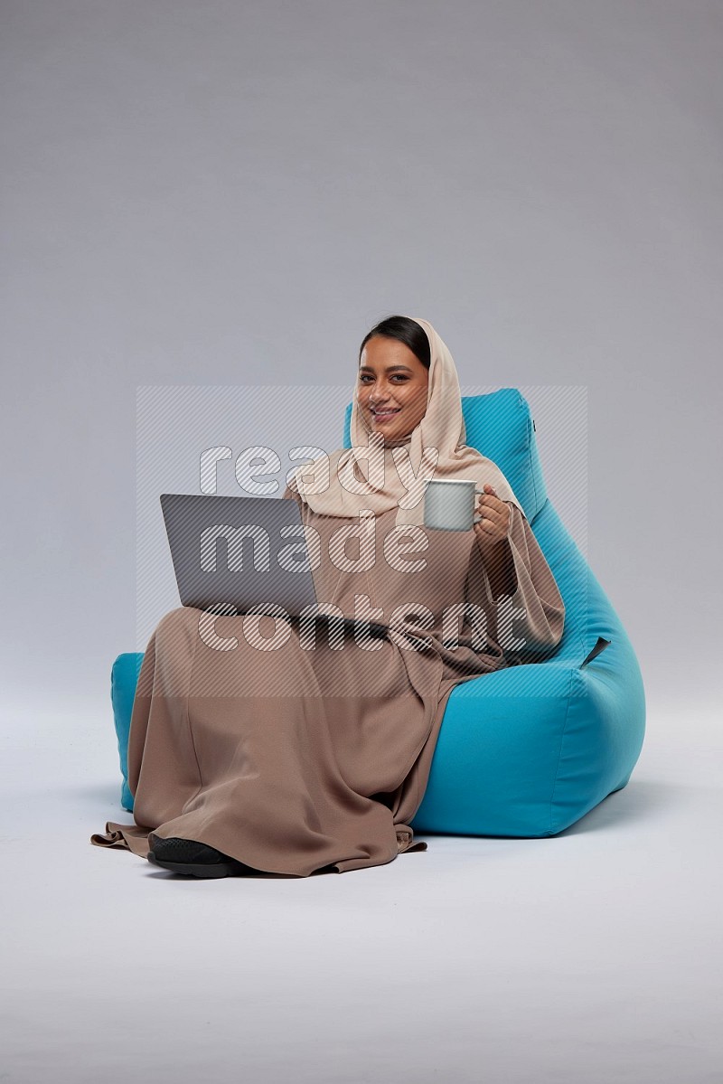 A Saudi woman sitting on a blue beanbag and working on laptop