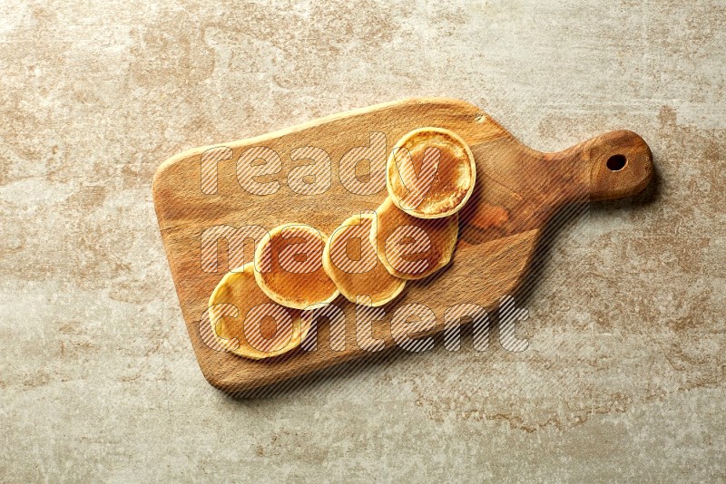 Five stacked plain mini pancakes on a wooden board on beige background