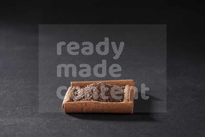 A single square of cinnamon sticks full of flaxseeds on black flooring