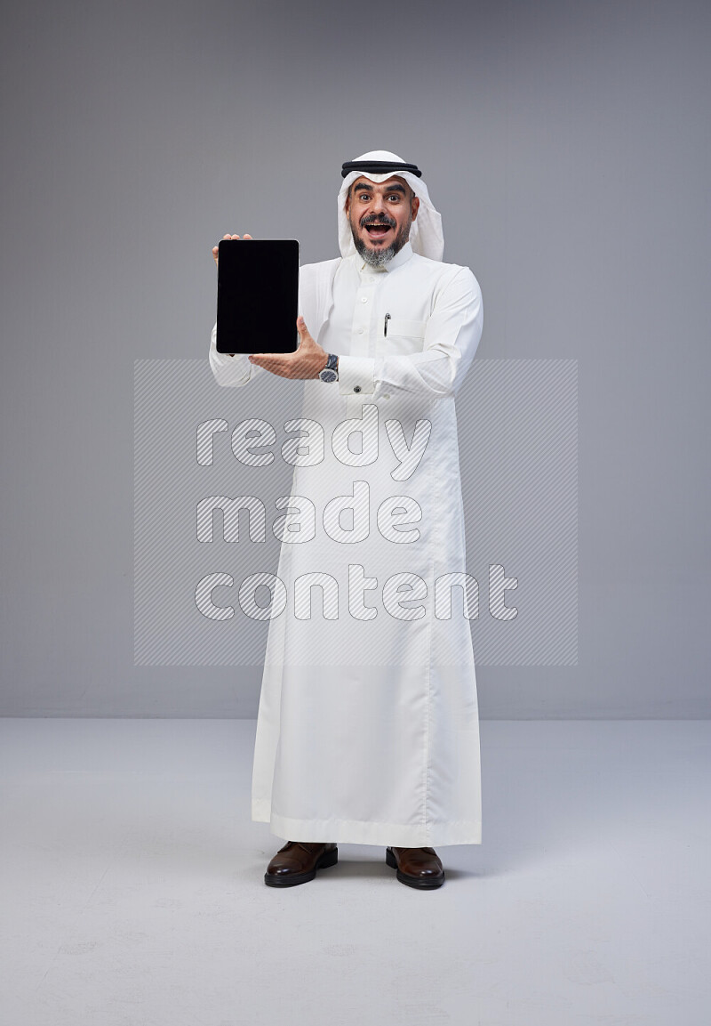 رجل سعودي يرتدي ثوب وشماغ ابيض ويحمل تابلت