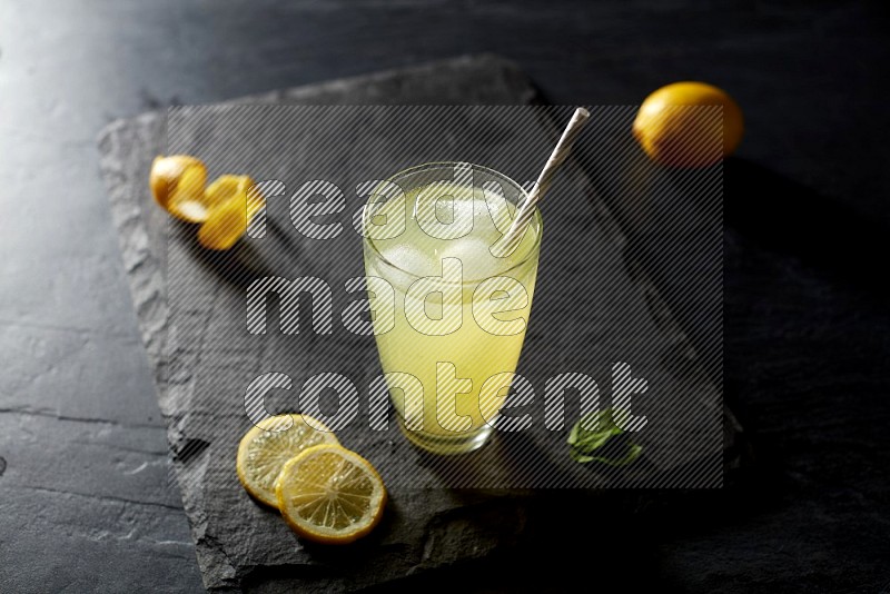 A glass of lemon juice with a straw on black background