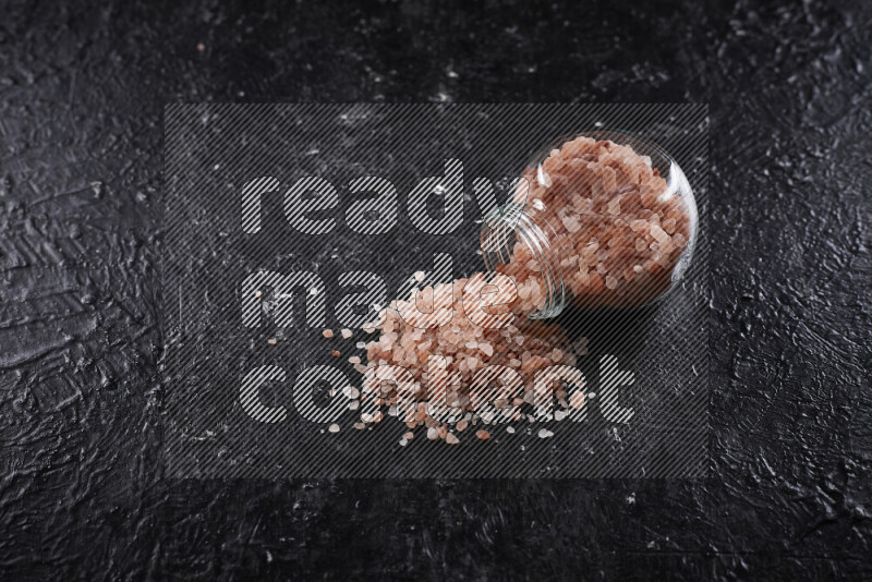 A glass jar full of coarse himalayan salt crystals on black background