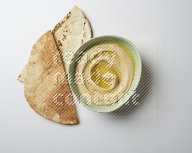 Hummus in a green plate garnished with olive oil on a white background