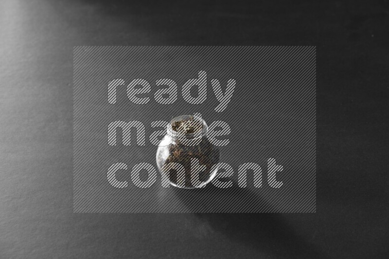 A glass spice jar full of basil on black flooring