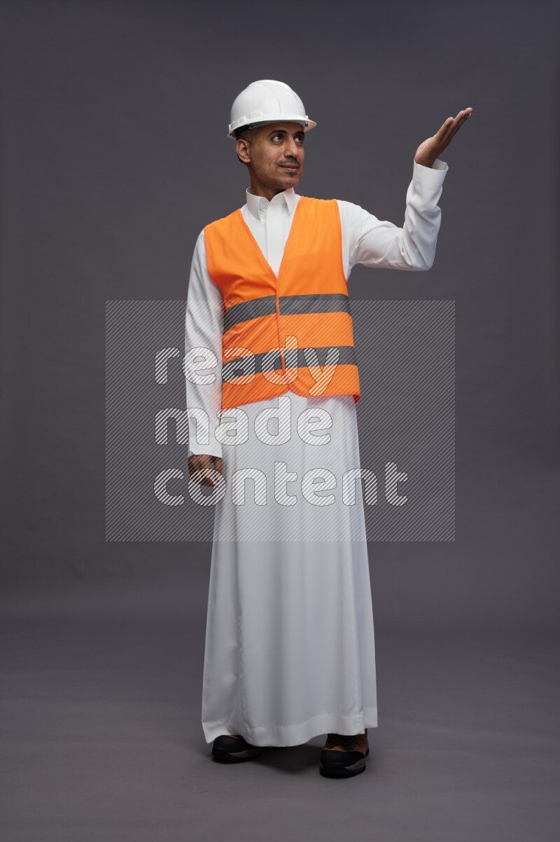 Saudi man wearing thob with engineer vest standing interacting with the camera on gray background
