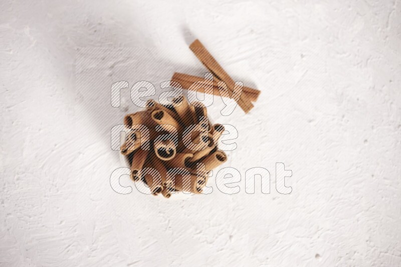Cinnamon sticks in a beige bowl on a white background