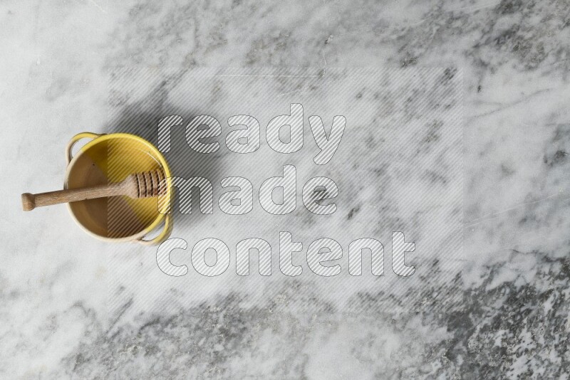 Multicolored pottery bowl with wooden honey dipper in it on grey marble background