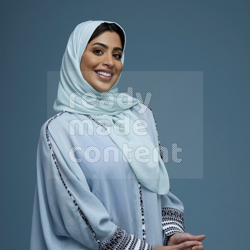 A woman posing in a blue background wearing a blue Abaya with hijab