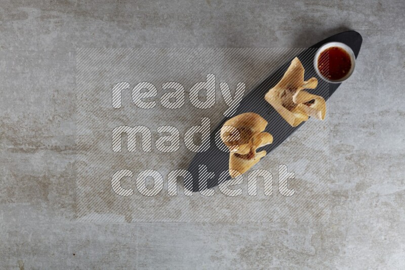 wonton cups with soy sauce ramkin on oval slate on grey textured counter top