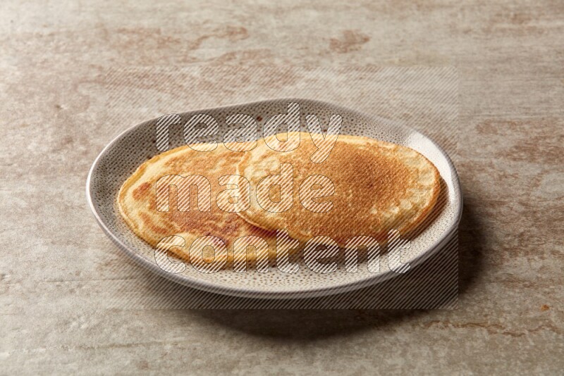 Two stacked plain pancakes in an irregular plate on beige background