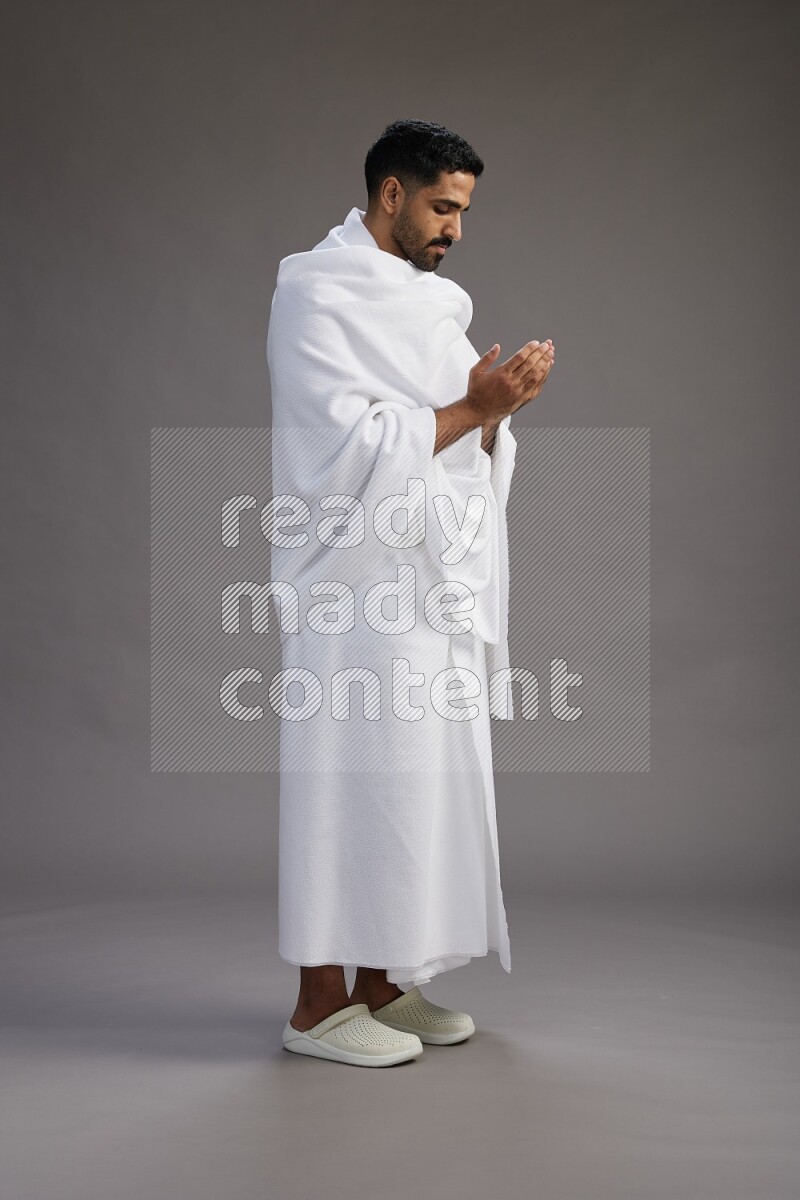 A man wearing Ehram Standing performing dua'a on gray background