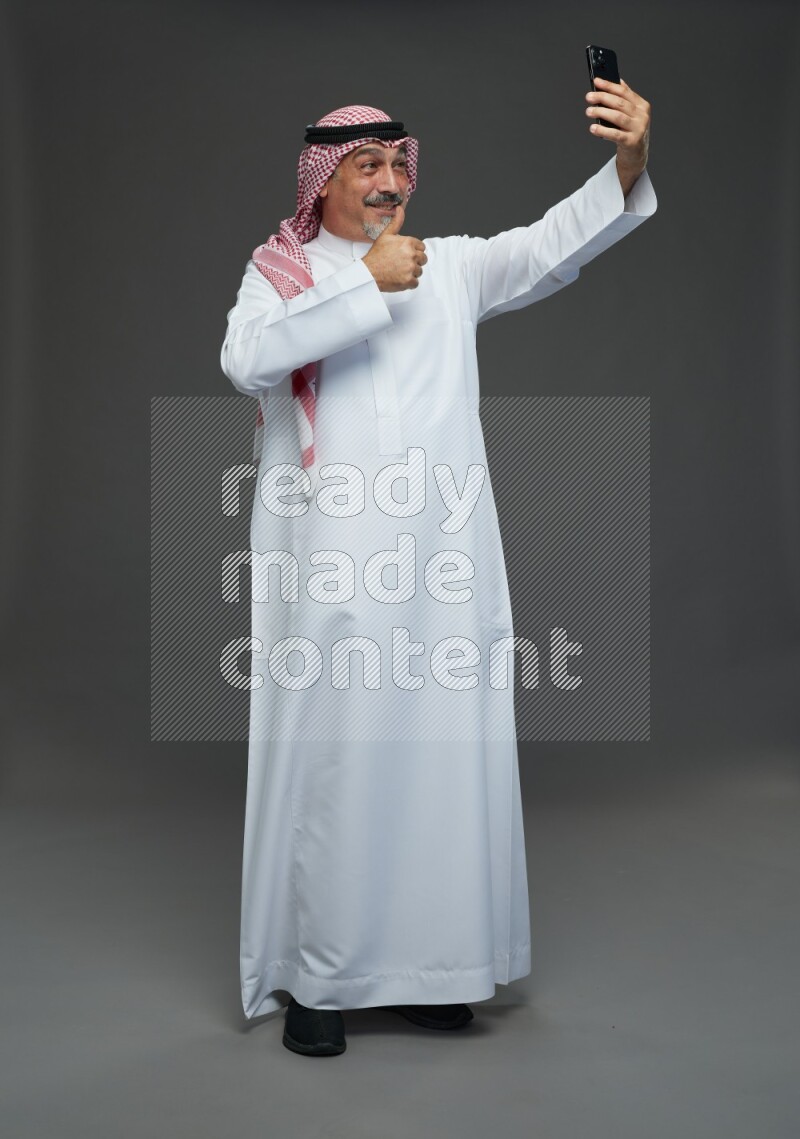 Saudi man with shomag Standing taking selfie on gray background