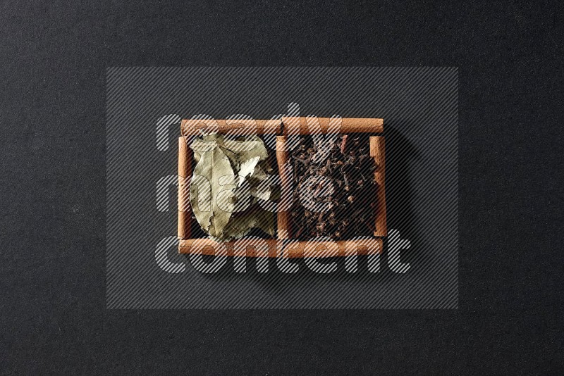 2 squares of cinnamon sticks full of cloves and bay laurel leaves on black flooring