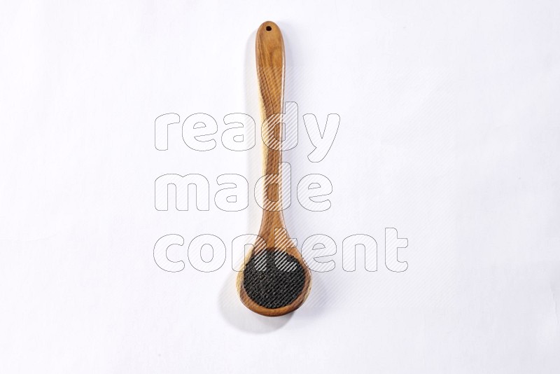 A wooden ladle full of black seeds on a white flooring