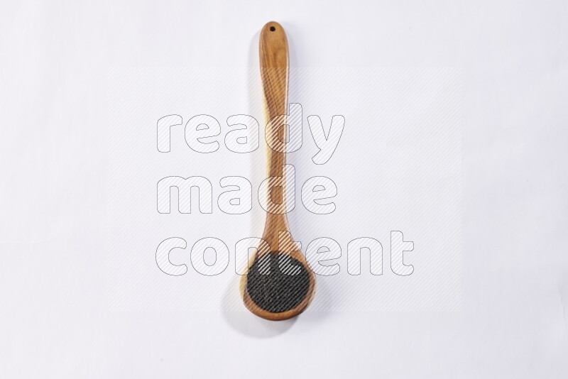 A wooden ladle full of black seeds on a white flooring