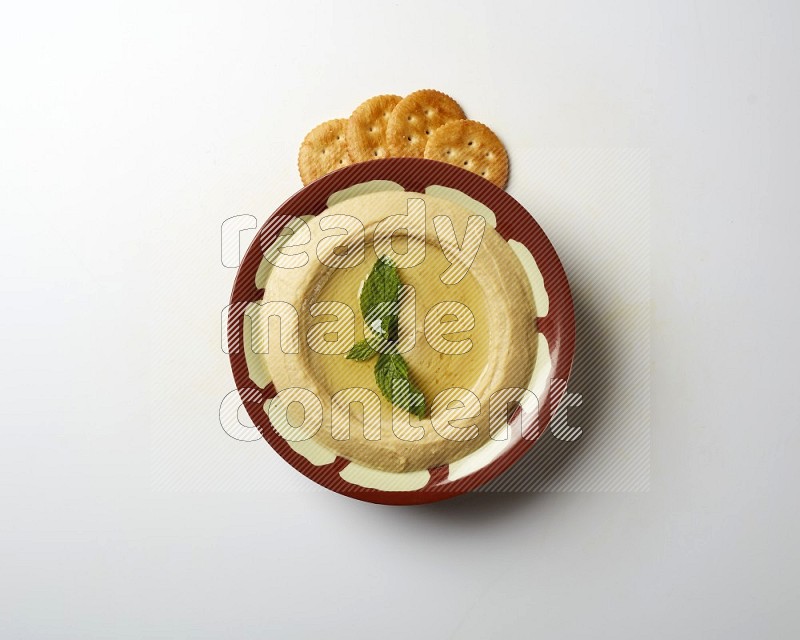 Hummus in a traditional plate garnished with mint on a white background