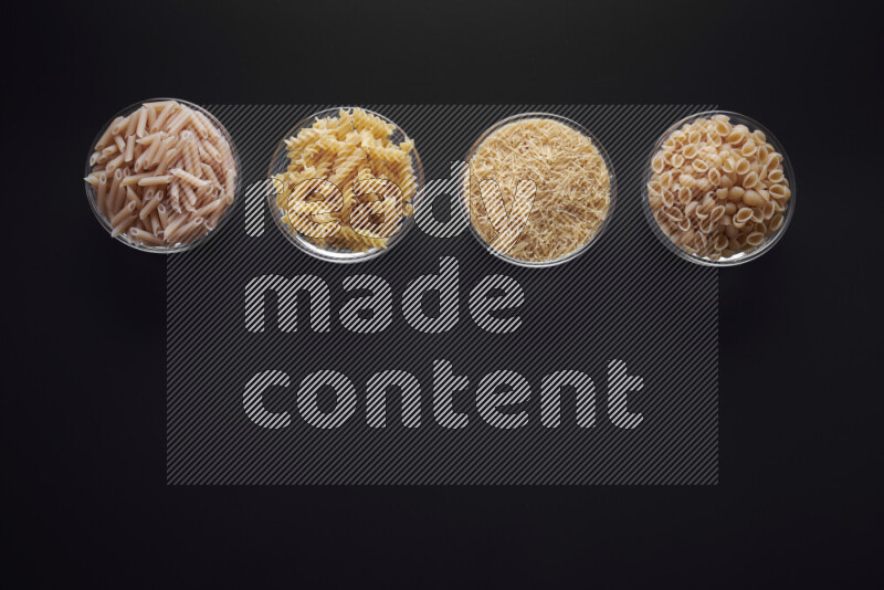 Different pasta types in glass bowls on black background