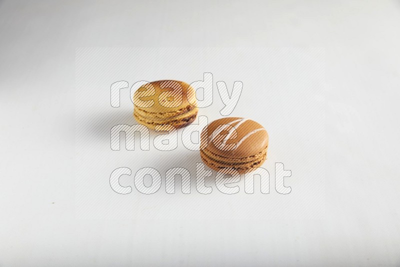 45º Shot of of two assorted Brown Irish Cream, and Yellow Crème Brulée macarons on white background