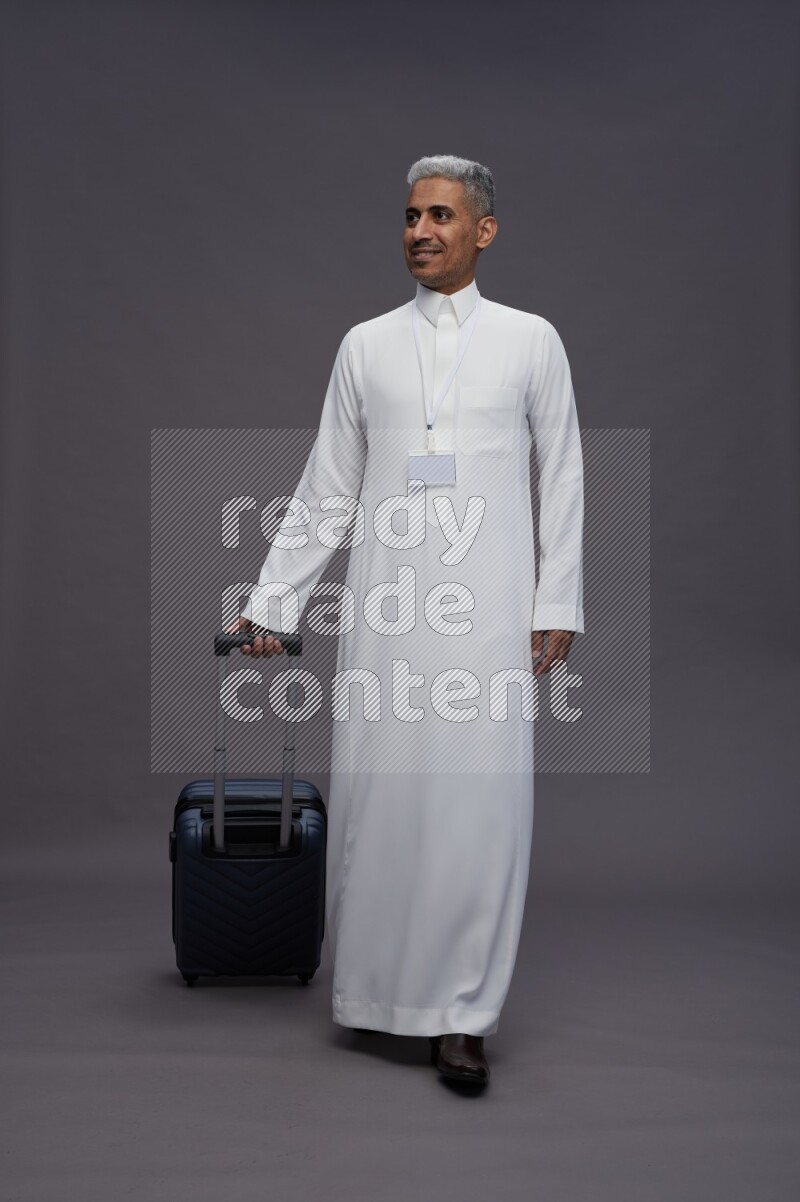 Saudi man wearing thob with neck strap employee badge standing holding bag on gray background