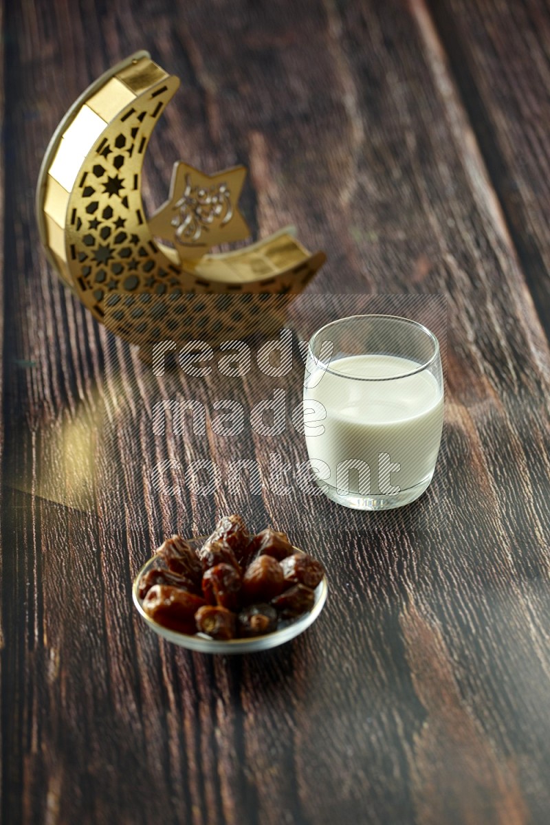 A crescent lantern with drinks, dates, nuts, prayer beads and quran on brown wooden background