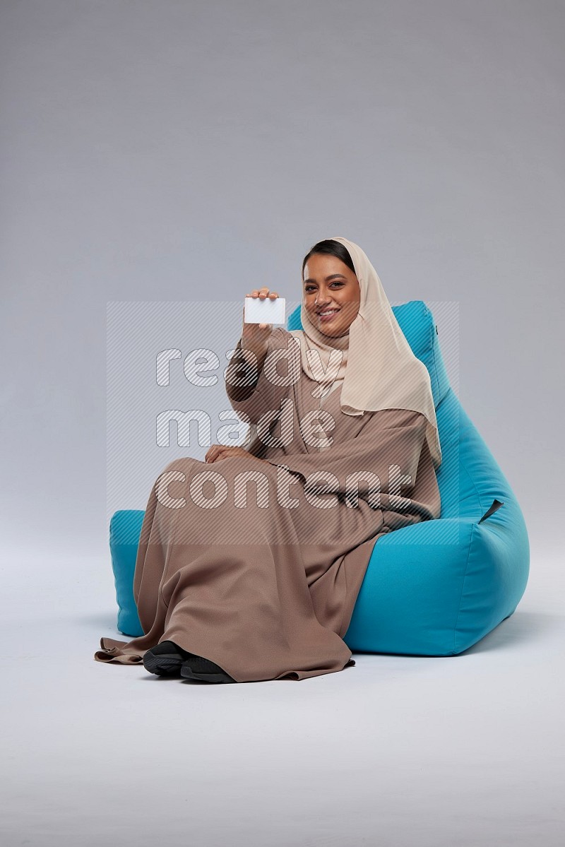 A Saudi woman sitting on a blue beanbag and holding ATM card