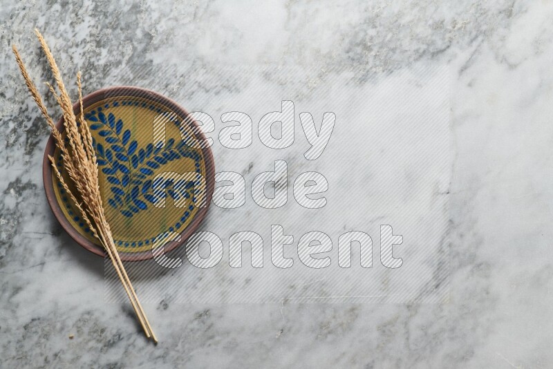 Wheat stalks on decorative pottery plate on grey marble background