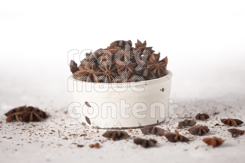 Star Anise in a white bowl and more of it sprinkled on white background